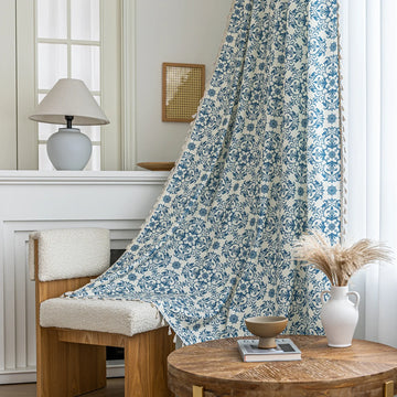 Elegant cream curtain fabric with intricate blue floral patterns, finished with decorative beige tassel trim for a classic, sophisticated look.