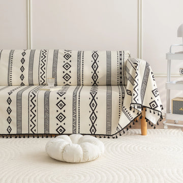 Modern black and white geometric patterned sofa cover with tribal-inspired diamond and stripe designs, accented by black tassel trim, adding a stylish and bohemian touch to living room décor.
