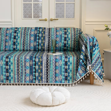 Vibrant sofa cover with blue, teal, and navy geometric tribal patterns, accented with white tassel trim, creating a bold and stylish statement for modern or bohemian living room décor.