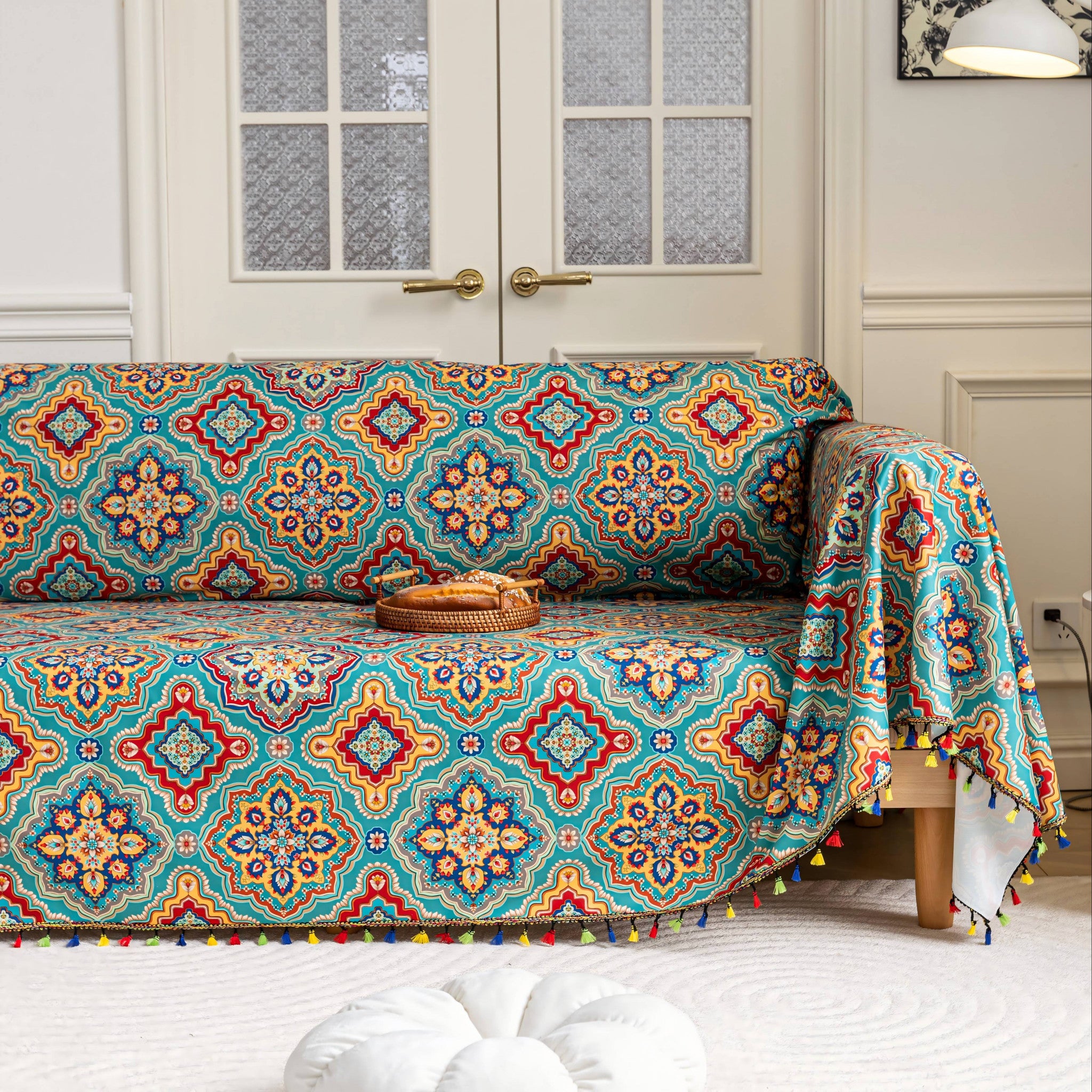 A vibrant, multicolored sofa cover featuring intricate geometric patterns in shades of red, blue, yellow, and green. The design includes detailed motifs and a playful fringe along the edges, adding a colorful and cozy touch to the living space.
