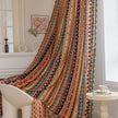 A vibrant curtain with a striking pattern of colorful stripes, featuring geometric shapes in red, orange, yellow, blue, and black. The curtain is adorned with playful tassels along the edges, adding a lively touch to the space.