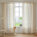 Colorful geometric patterned curtain with rows of blue, yellow, and red shapes beside a window, styled with a tasseled edge.