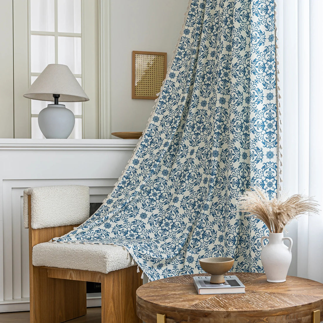Elegant cream curtain fabric with intricate blue floral patterns, finished with decorative beige tassel trim for a classic, sophisticated look.