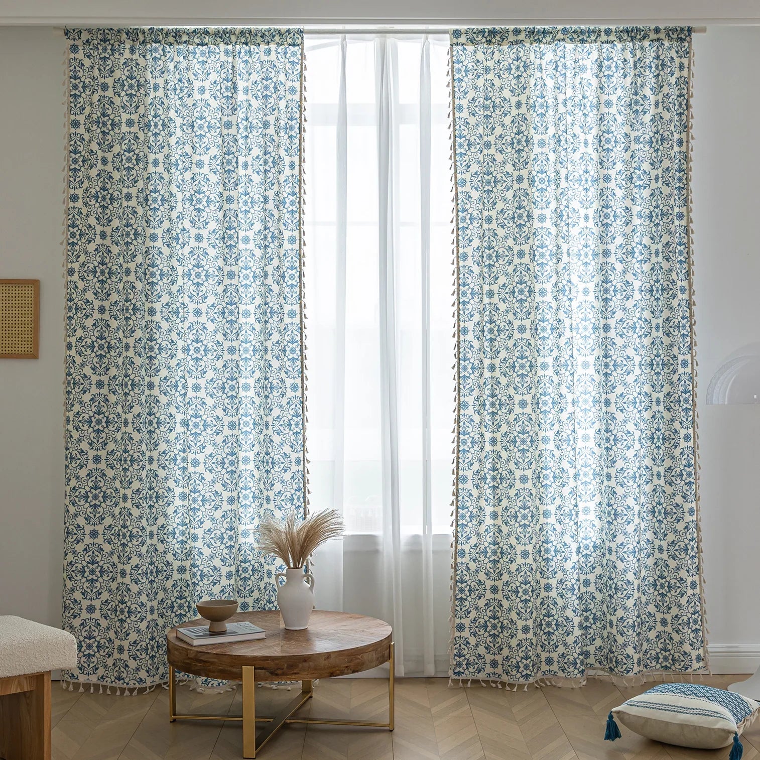 Elegant cream curtain fabric with intricate blue floral patterns, finished with decorative beige tassel trim for a classic, sophisticated look.