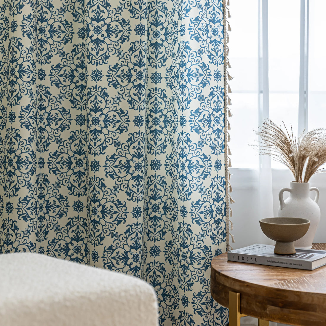 Elegant cream curtain fabric with intricate blue floral patterns, finished with decorative beige tassel trim for a classic, sophisticated look.