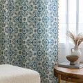Elegant cream curtain fabric with intricate blue floral patterns, finished with decorative beige tassel trim for a classic, sophisticated look.