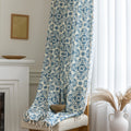 Elegant cream curtain fabric with intricate blue floral patterns, finished with decorative beige tassel trim for a classic, sophisticated look.