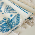 Close-up of cream curtain fabric with intricate blue tribal and geometric patterns, finished with decorative beige tassel trim for a stylish bohemian look.