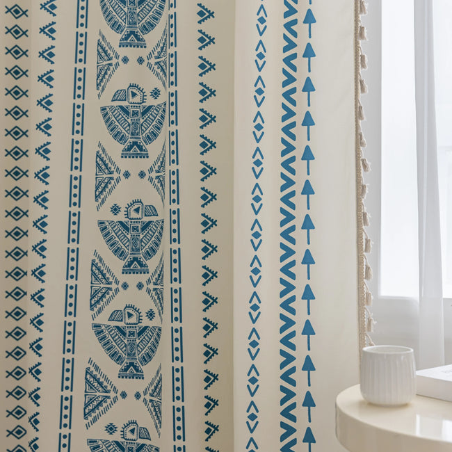 Cream curtain fabric with intricate blue tribal and geometric patterns, finished with decorative beige tassel trim for a stylish bohemian look.