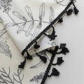 Cream curtains with black botanical print and black tassel trim.
