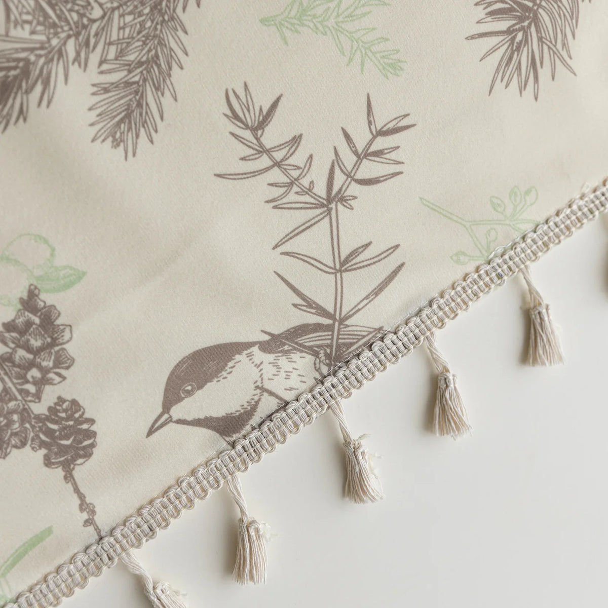 Close-up of beige curtain with bird and botanical print in brown and green, featuring decorative tassel trim for a rustic, nature-inspired look.