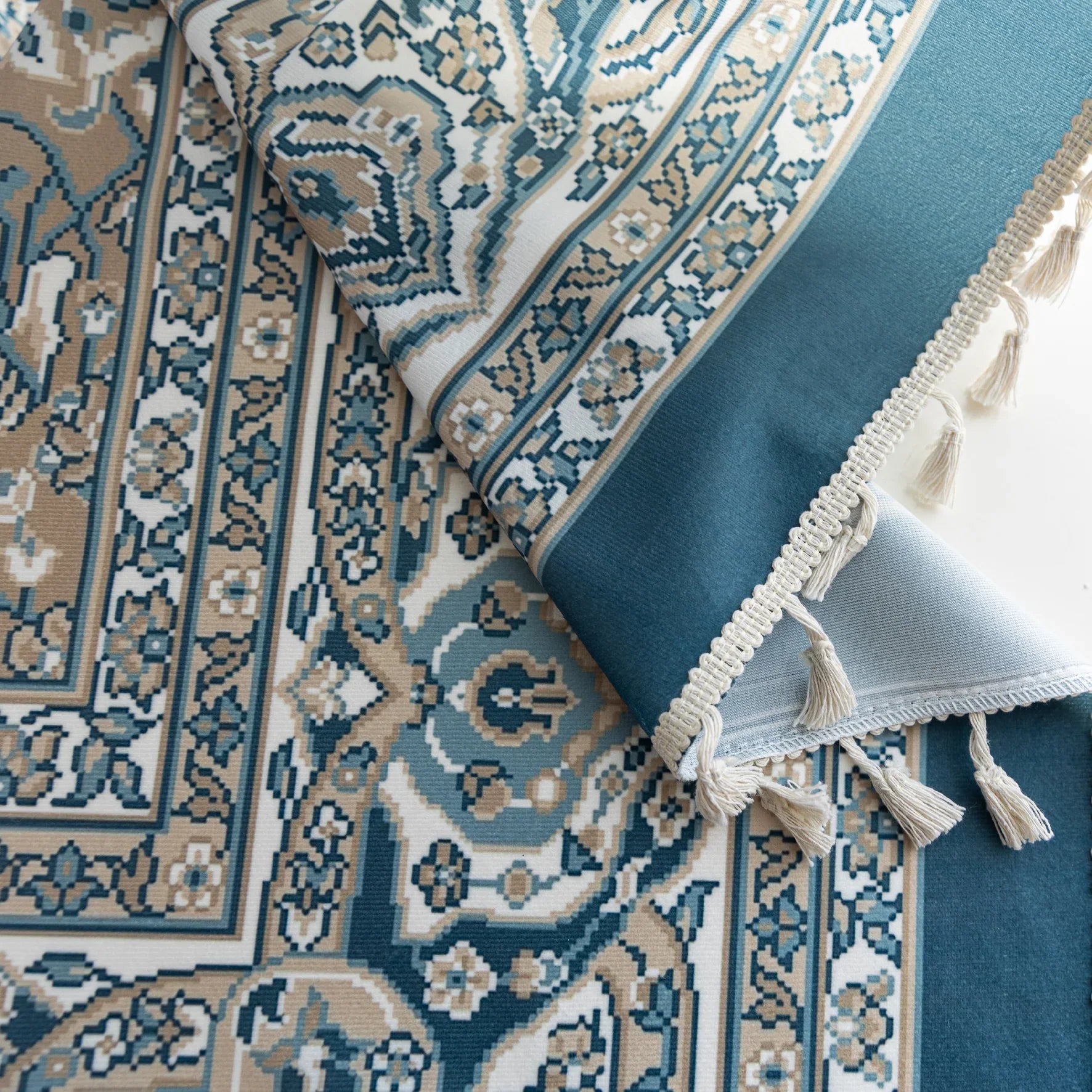 Close-up of blue and beige curtain fabric with intricate Persian-inspired floral patterns, featuring decorative tassel trim for an elegant and classic home décor look.