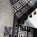 Close-up of black and white curtain fabric with Greek key pattern and floral accents, featuring decorative black tassel trim for a bold and elegant home décor style.