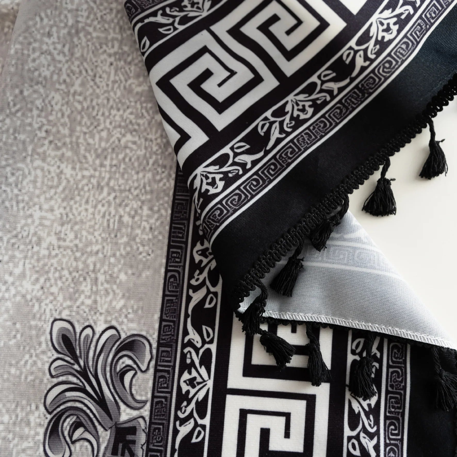 Close-up of black and white curtain fabric with Greek key pattern and floral accents, featuring decorative black tassel trim for a bold and elegant home décor style.