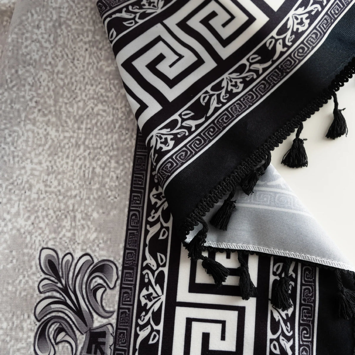 Close-up of black and white curtain fabric with Greek key pattern and floral accents, featuring decorative black tassel trim for a bold and elegant home d¨¦cor style.