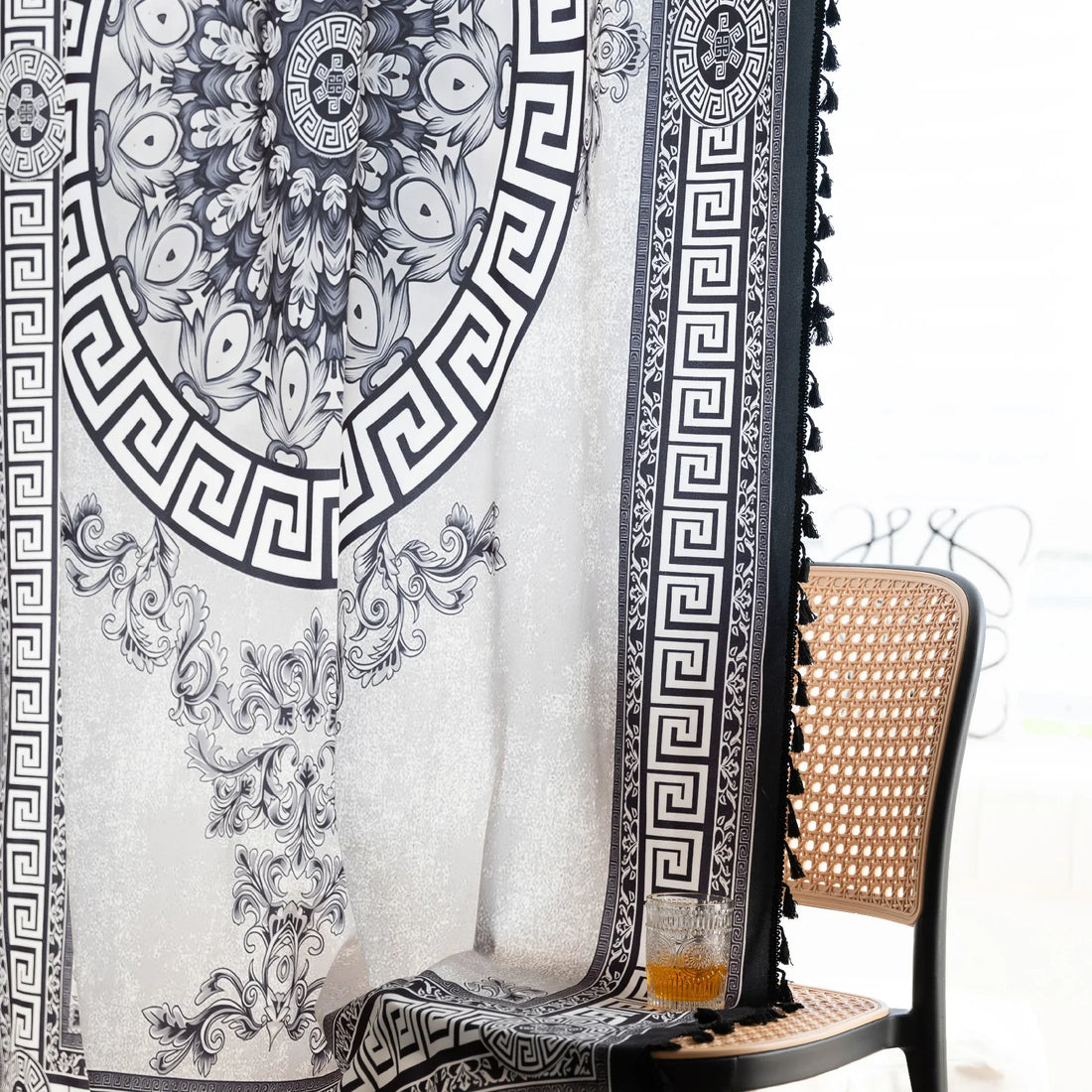 Black and white curtain fabric with Greek key pattern and floral accents, featuring decorative black tassel trim for a bold and elegant home décor style.