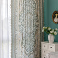 Close-up of an ornate curtain featuring a green background with intricate white floral and medallion patterns, accented with beige and gold details for a vintage, luxurious home décor style.