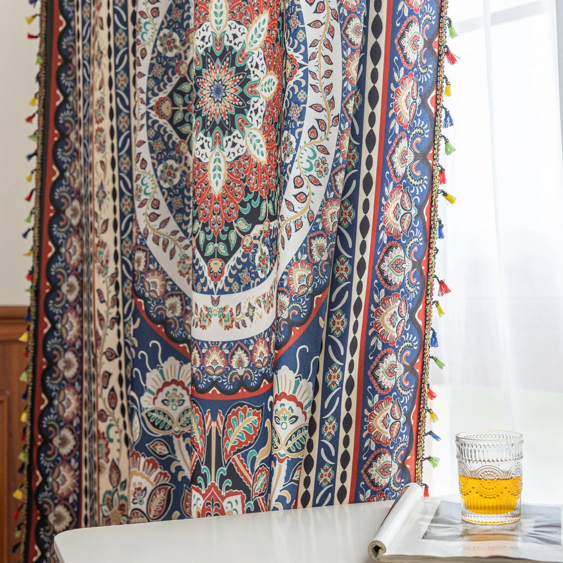 Colorful bohemian curtain with intricate floral and medallion patterns in navy blue, red, green, and cream, adorned with multicolored tassels.