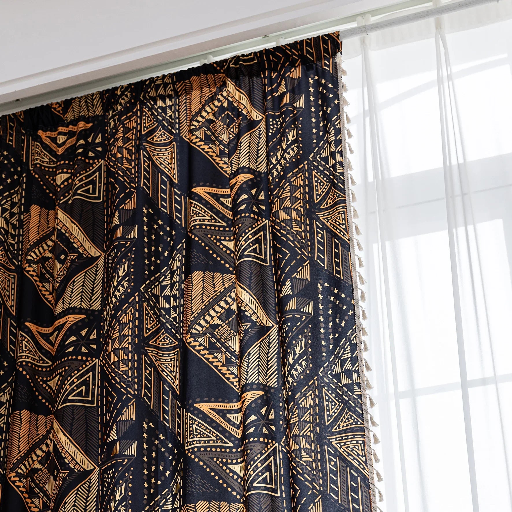 Stylish ethnic-inspired curtain with bold geometric patterns in warm golden-orange tones on a deep black background, accented with delicate tassel trim — ideal for adding a modern tribal touch and cozy elegance to your living space.
