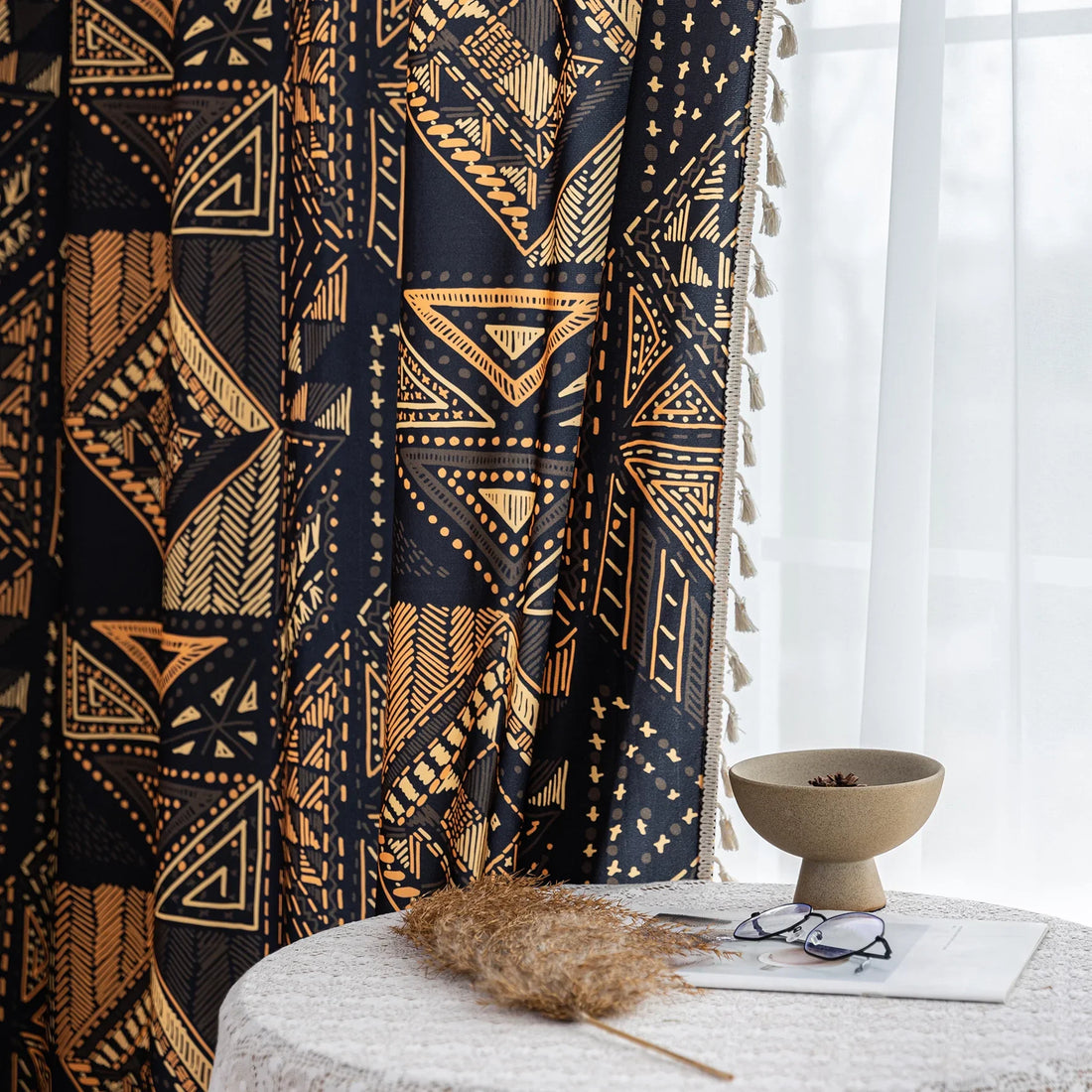 Stylish ethnic-inspired curtain with bold geometric patterns in warm golden-orange tones on a deep black background, accented with delicate tassel trim — ideal for adding a modern tribal touch and cozy elegance to your living space.