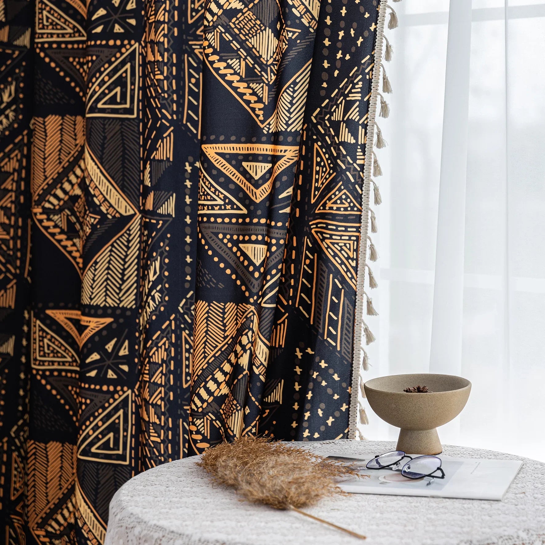 Stylish ethnic-inspired curtain with bold geometric patterns in warm golden-orange tones on a deep black background, accented with delicate tassel trim — ideal for adding a modern tribal touch and cozy elegance to your living space.