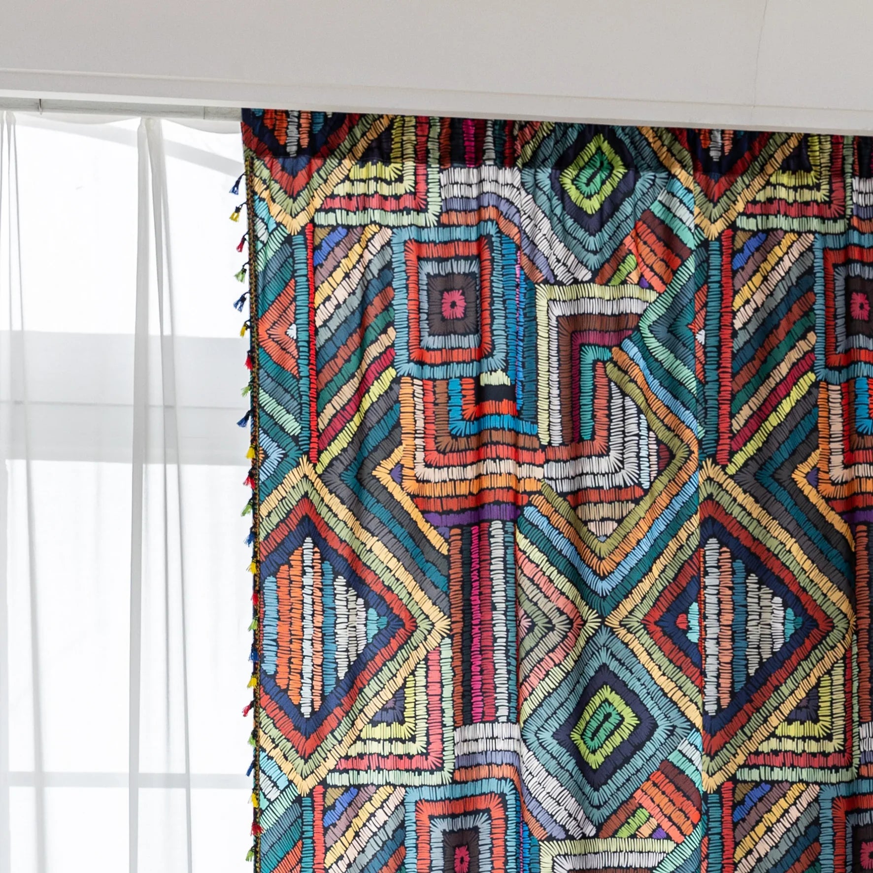 Vibrant geometric bohemian curtain with bold multicolor diamond patterns, featuring intricate woven-style designs and colorful tassel trim — ideal for adding a lively, artistic statement to any room décor.