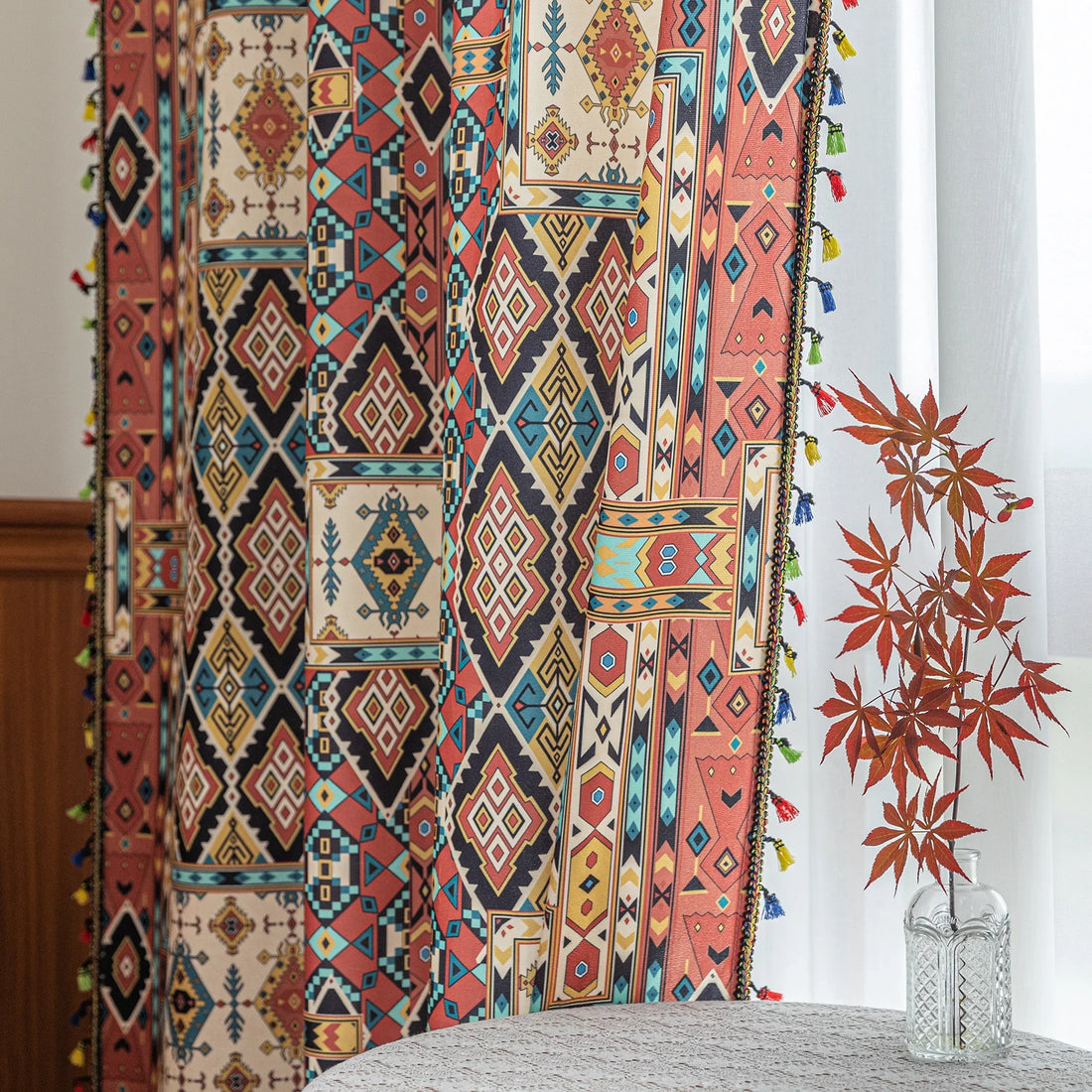 Colorful bohemian curtain with intricate tribal geometric patterns in rich earthy tones of red, beige, turquoise, and gold, accented with multicolor tassels — a perfect choice to add warmth, texture, and global-inspired charm to any room décor.