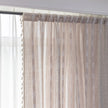 Khaki and white embroidered curtain hanging by a window