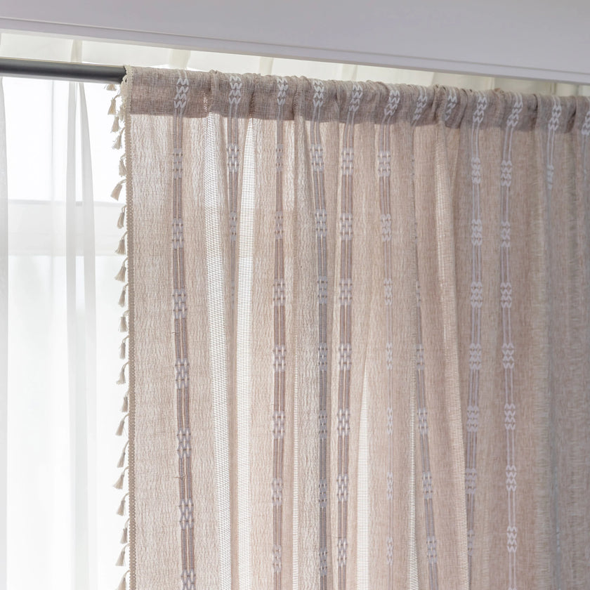 Khaki and white embroidered curtain hanging by a window