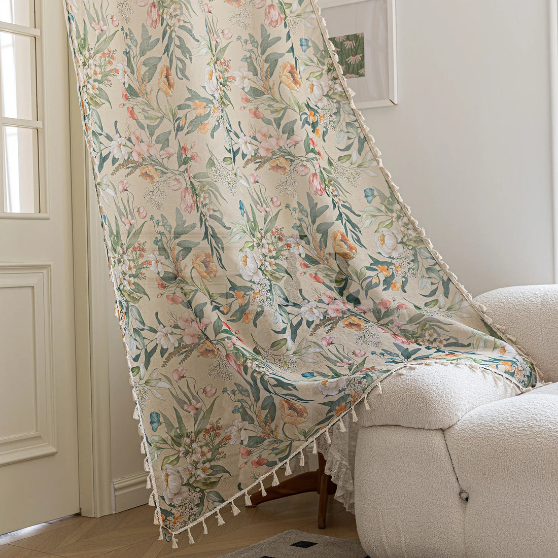 Close-up of beige sheer curtain with colorful floral and leafy pattern, decorated with delicate tassel trim, creating an elegant and airy botanical look for home interiors.