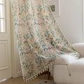 Close-up of beige sheer curtain with colorful floral and leafy pattern, decorated with delicate tassel trim, creating an elegant and airy botanical look for home interiors.