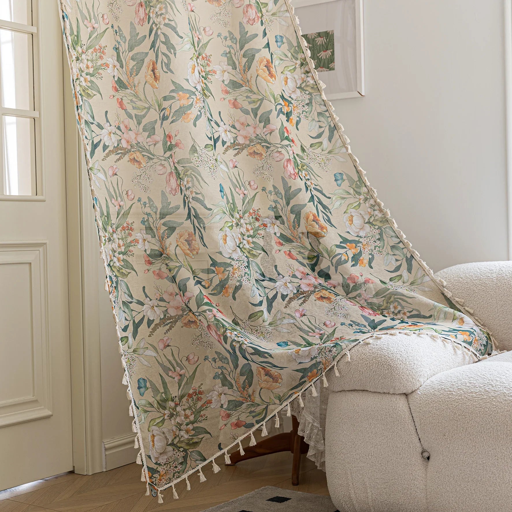 Close-up of beige sheer curtain with colorful floral and leafy pattern, decorated with delicate tassel trim, creating an elegant and airy botanical look for home interiors.