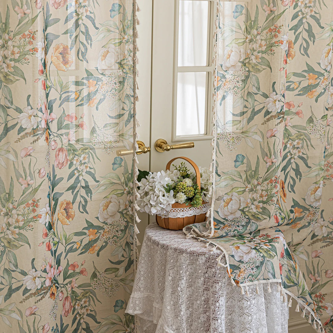 Close-up of beige sheer curtain with colorful floral and leafy pattern, decorated with delicate tassel trim, creating an elegant and airy botanical look for home interiors.