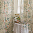Close-up of beige sheer curtain with colorful floral and leafy pattern, decorated with delicate tassel trim, creating an elegant and airy botanical look for home interiors.