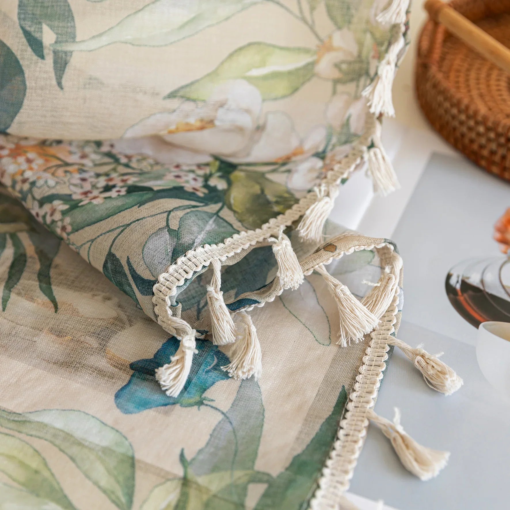 Close-up of beige sheer curtain with colorful floral and leafy pattern, decorated with delicate tassel trim, creating an elegant and airy botanical look for home interiors.