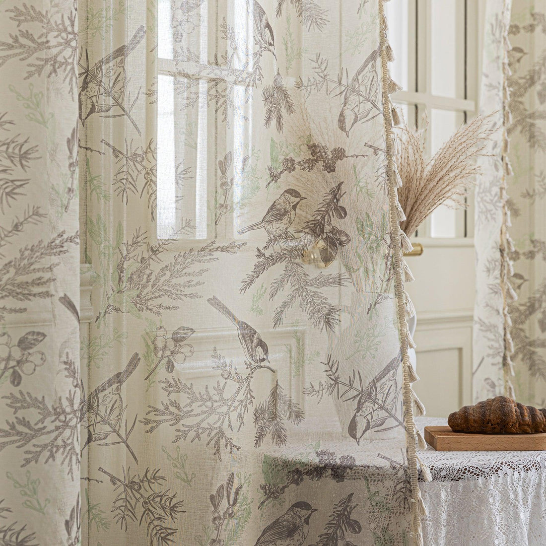 Beige curtain with delicate bird and botanical print in soft brown and green tones, finished with tassel trim, adding a rustic and nature-inspired charm to living room décor.
