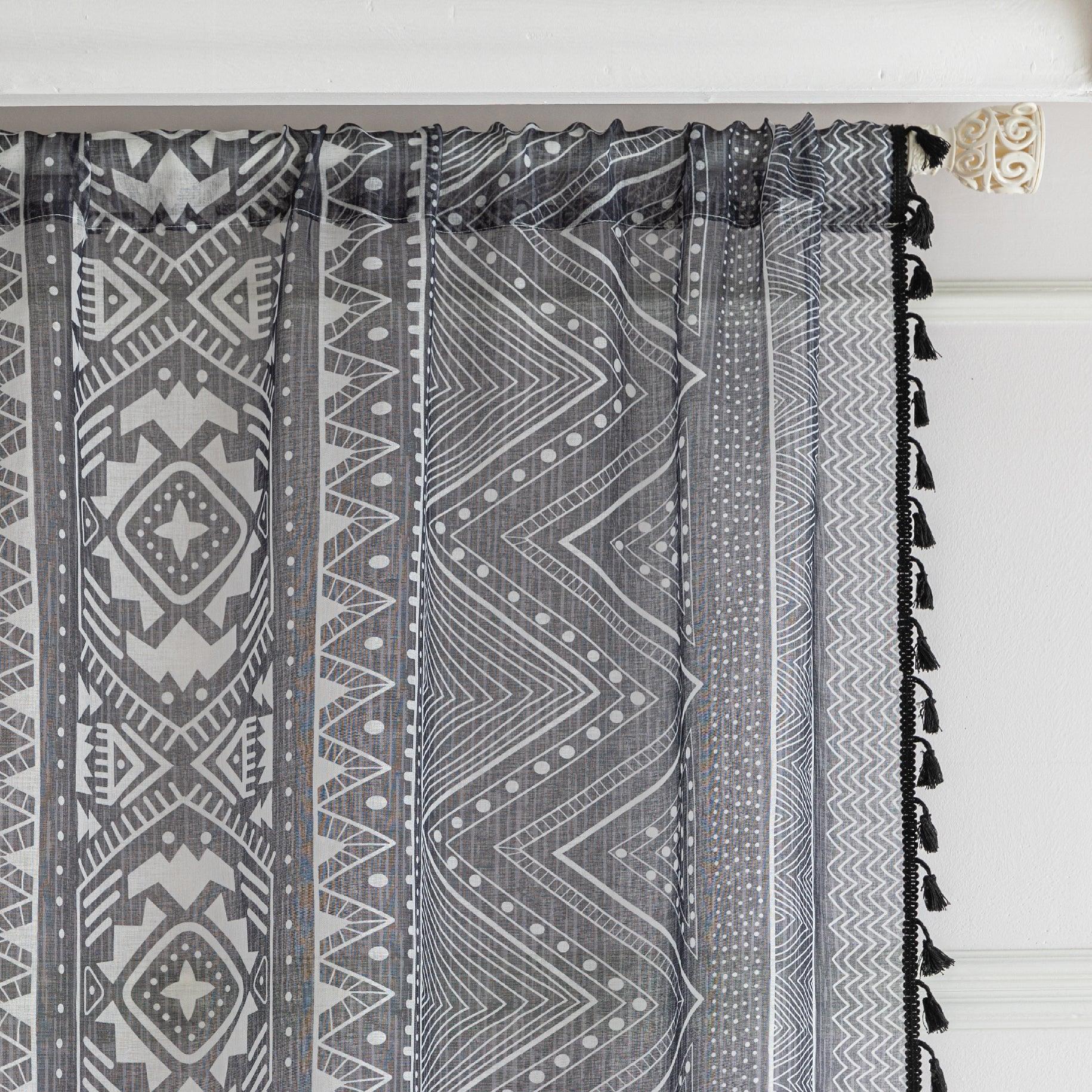 Modern Black and White Geometric Sheer Curtains – Enhance your home with these contemporary sheer curtains featuring an intricate tribal-inspired geometric pattern in black and white. The lightweight fabric allows natural light to filter through while maintaining a sense of privacy, making them perfect for living rooms, bedrooms, or minimalist interiors. Finished with delicate black tassels along the edges, these curtains add a stylish yet subtle decorative touch that complements modern, boho, or Scandinavi