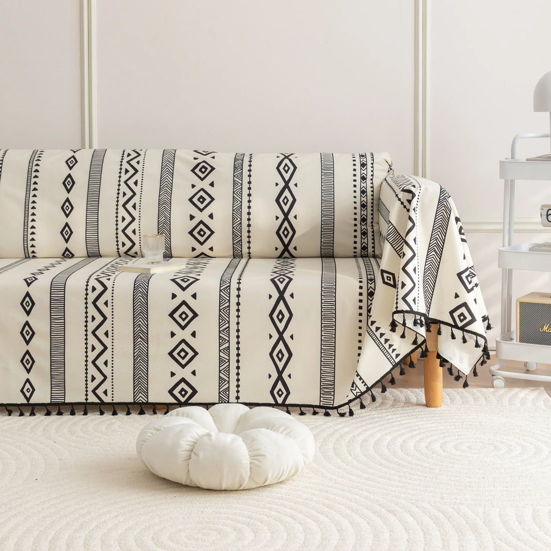 Modern black and white geometric patterned sofa cover with tribal-inspired diamond and stripe designs, accented by black tassel trim, adding a stylish and bohemian touch to living room décor.