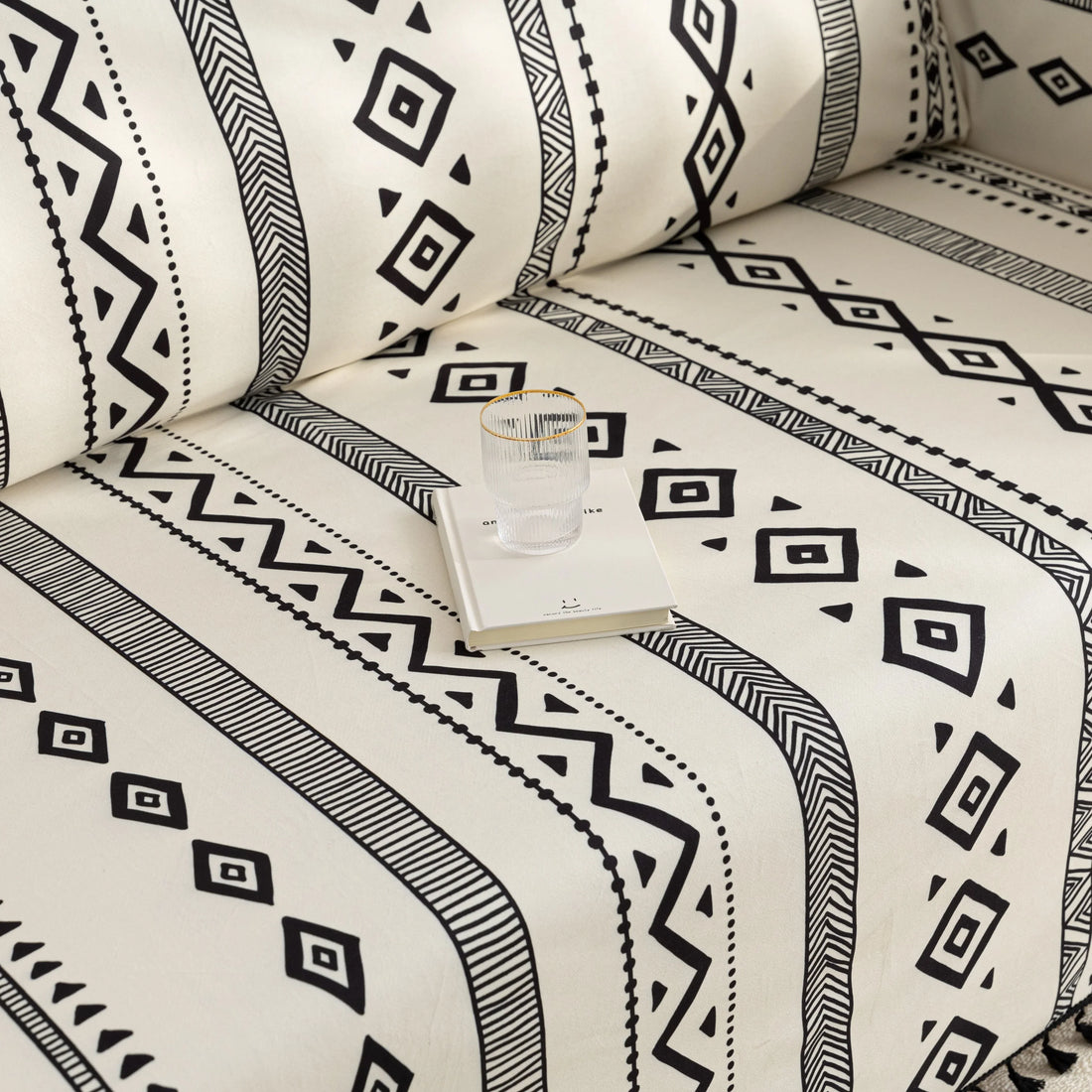 Modern black and white geometric patterned sofa cover with tribal-inspired diamond and stripe designs, accented by black tassel trim, adding a stylish and bohemian touch to living room décor.