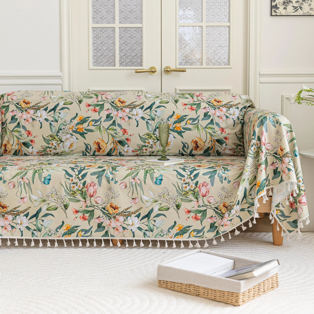 Beige floral sofa cover with vibrant botanical patterns in green, pink, yellow, and white, accented with delicate white tassel trim.