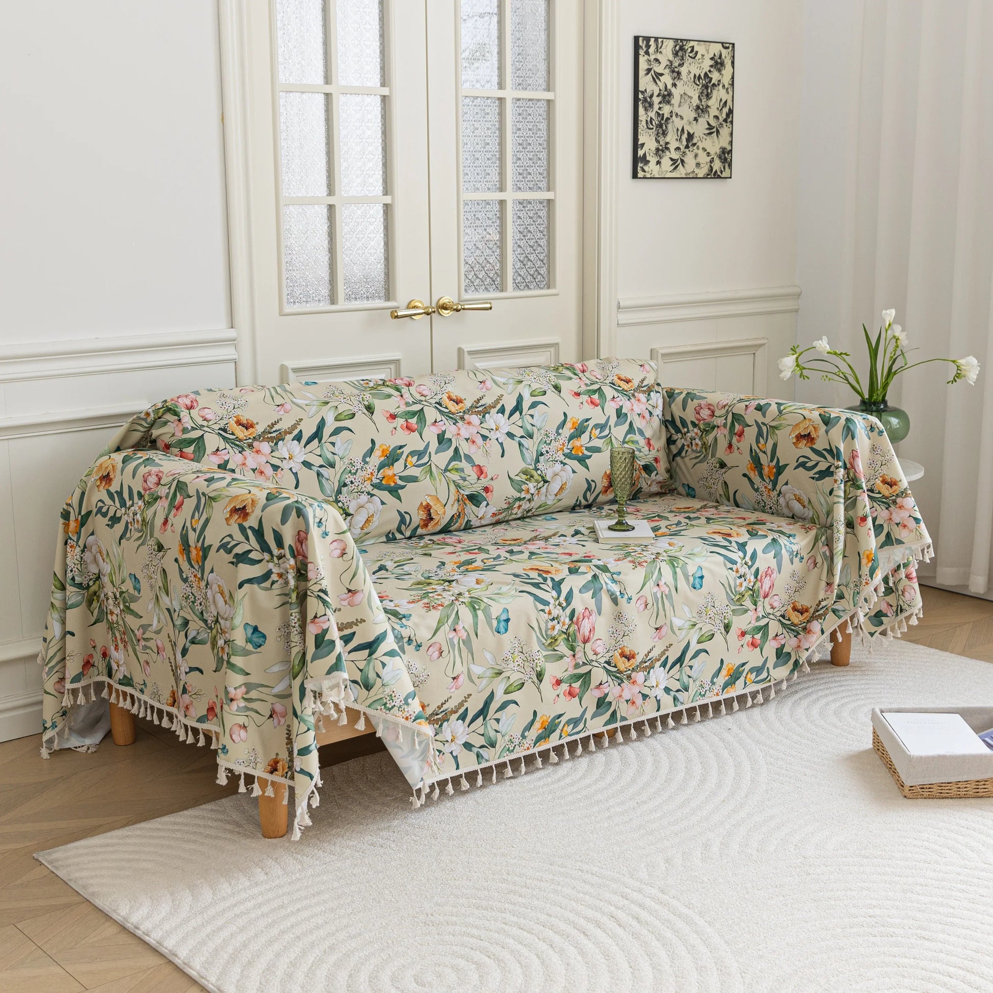 Beige floral sofa cover with vibrant botanical patterns in green, pink, yellow, and white, accented with delicate white tassel trim.