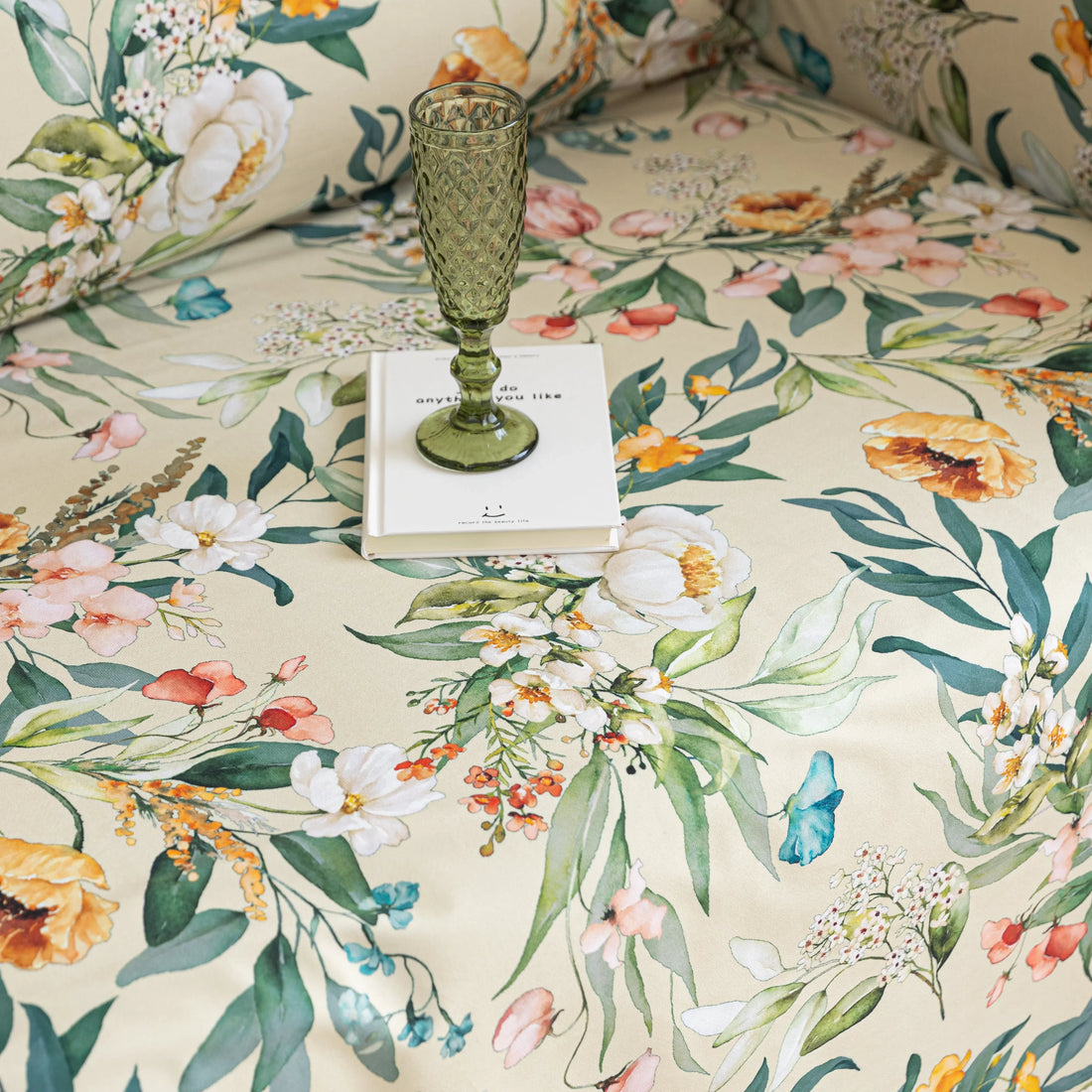 Beige floral sofa cover with vibrant botanical patterns in green, pink, yellow, and white, accented with delicate white tassel trim.