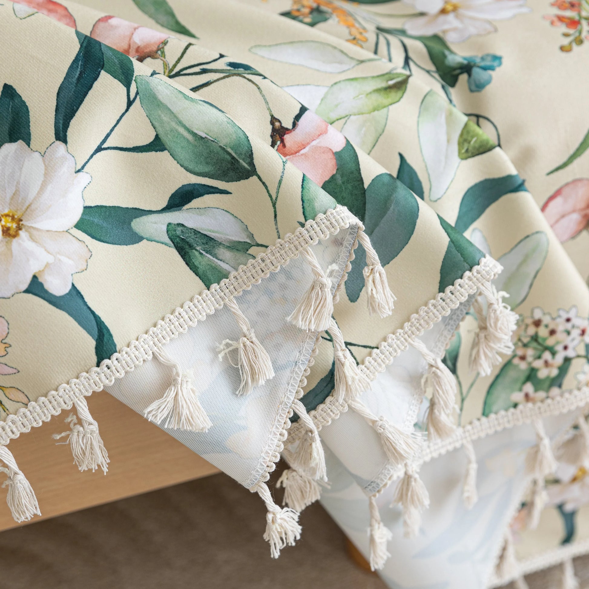 Beige floral sofa cover with vibrant botanical patterns in green, pink, yellow, and white, accented with delicate white tassel trim.
