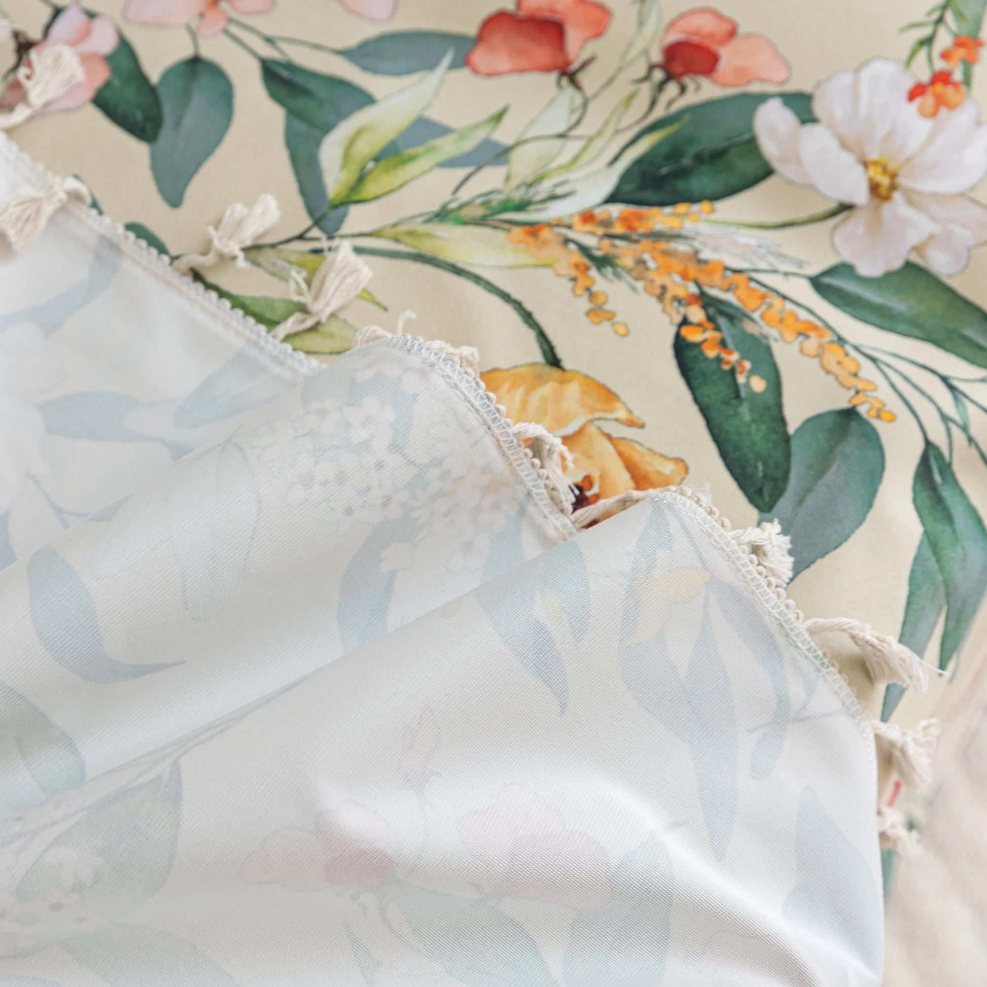 Beige floral sofa cover with vibrant botanical patterns in green, pink, yellow, and white, accented with delicate white tassel trim.