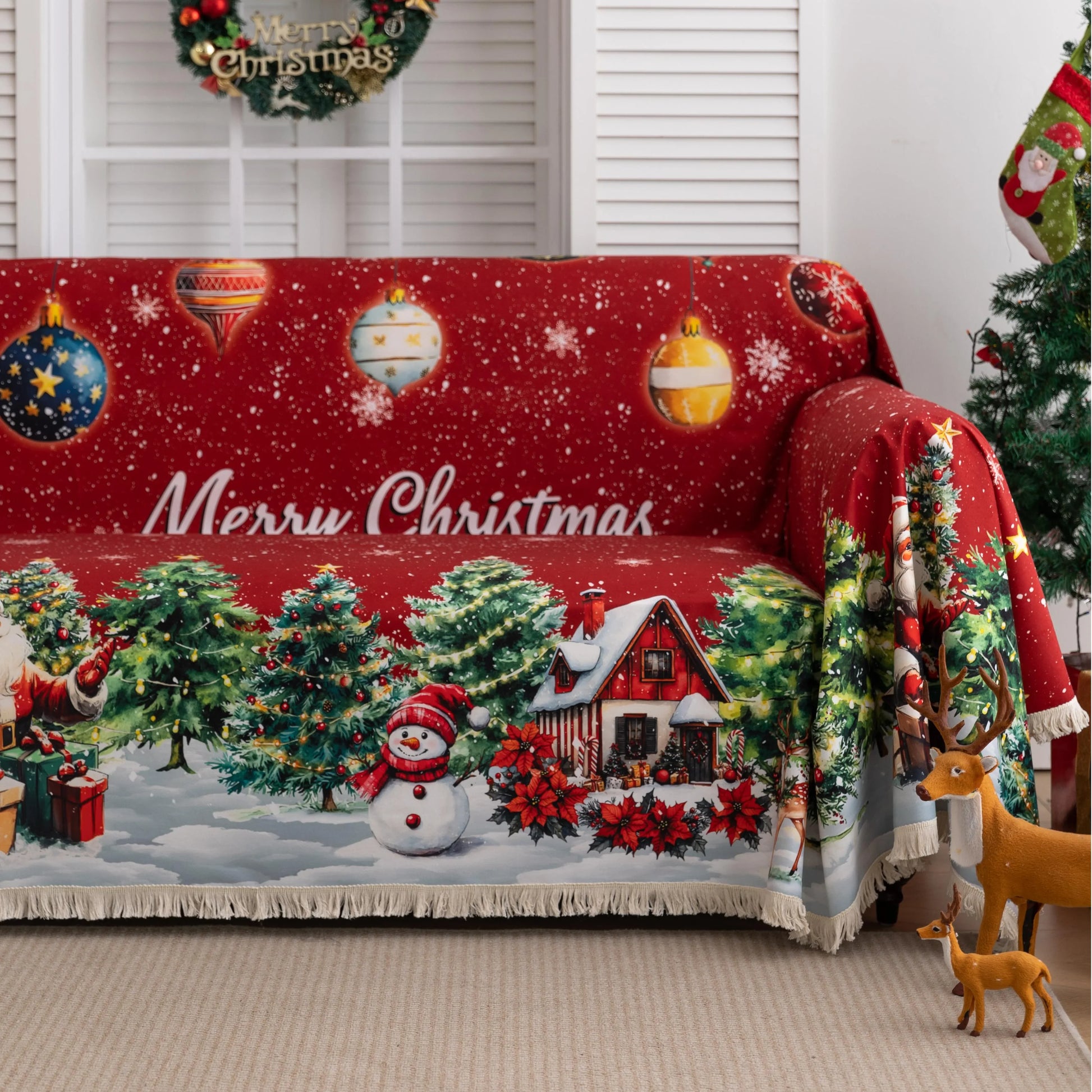 Festive red Christmas-themed sofa cover featuring decorated ornaments, snowflakes, snowy pine trees, a cheerful snowman, Santa Claus with gifts, and a cozy snow-covered house with poinsettias in the foreground.