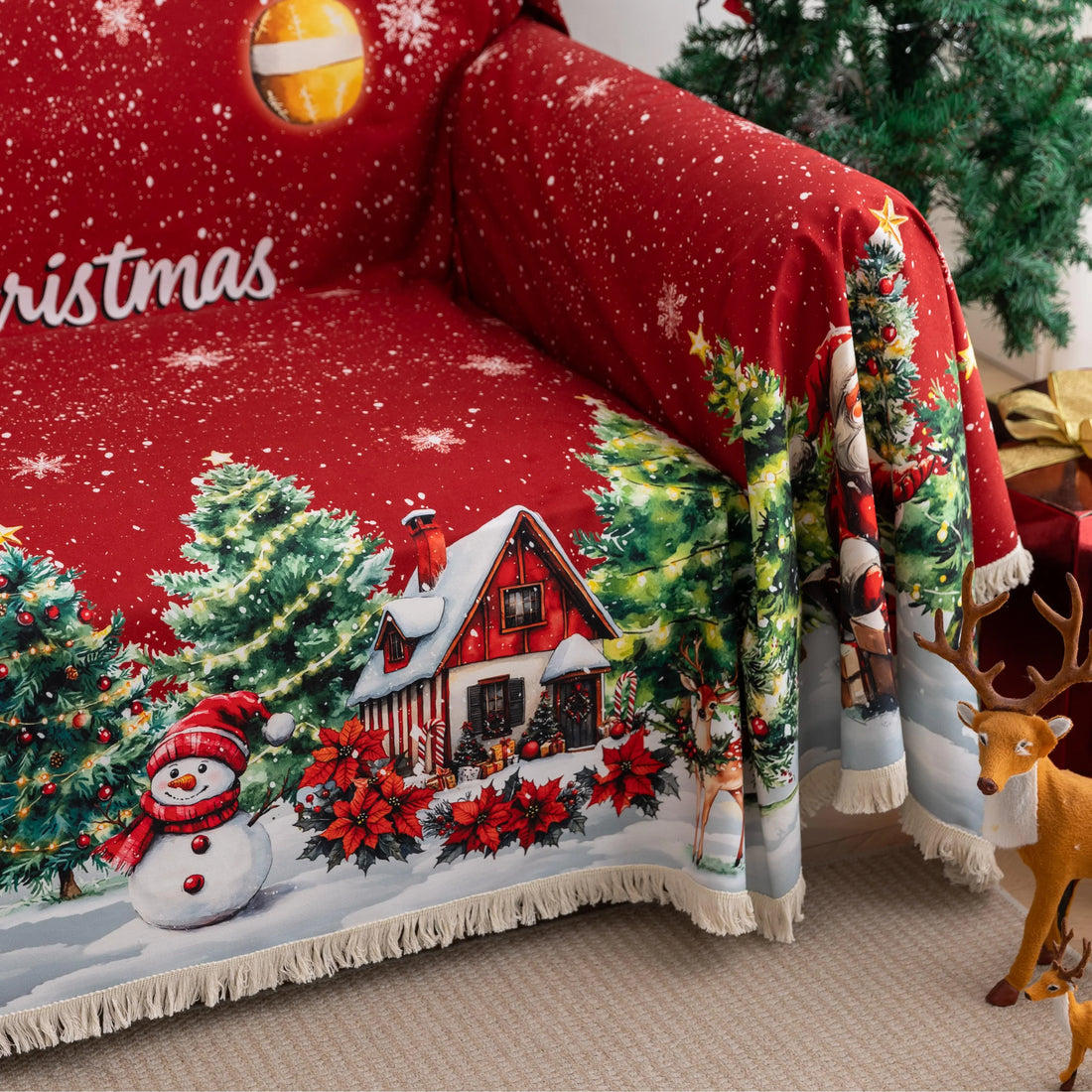 Festive red Christmas-themed sofa cover featuring decorated ornaments, snowflakes, snowy pine trees, a cheerful snowman, Santa Claus with gifts, and a cozy snow-covered house with poinsettias in the foreground.