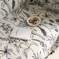 Elegant sofa cover with black botanical floral print on a cream background, featuring. delicate line-drawn flowers and plants with black tassel trim