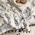 Elegant sofa cover with black botanical floral print on a cream background, featuring. delicate line-drawn flowers and plants with black tassel trim