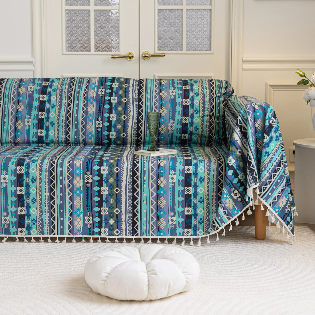 Vibrant sofa cover with blue, teal, and navy geometric tribal patterns, accented with white tassel trim, creating a bold and stylish statement for modern or bohemian living room décor.