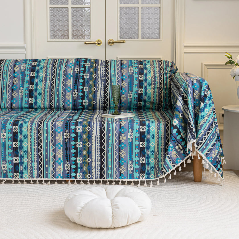 Vibrant sofa cover with blue, teal, and navy geometric tribal patterns, accented with white tassel trim, creating a bold and stylish statement for modern or bohemian living room d¨¦cor.